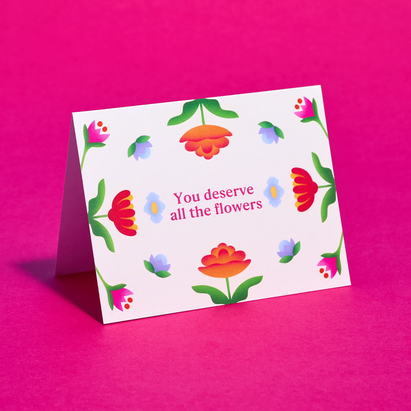 Greeting card with floral design and 'You deserve all the flowers' text on a pink background
