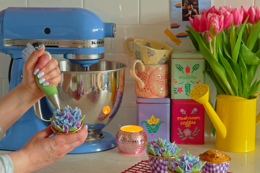 Hands pipe buttercream flower cupcakes in a colorful kitchen with fresh flowers and floral details