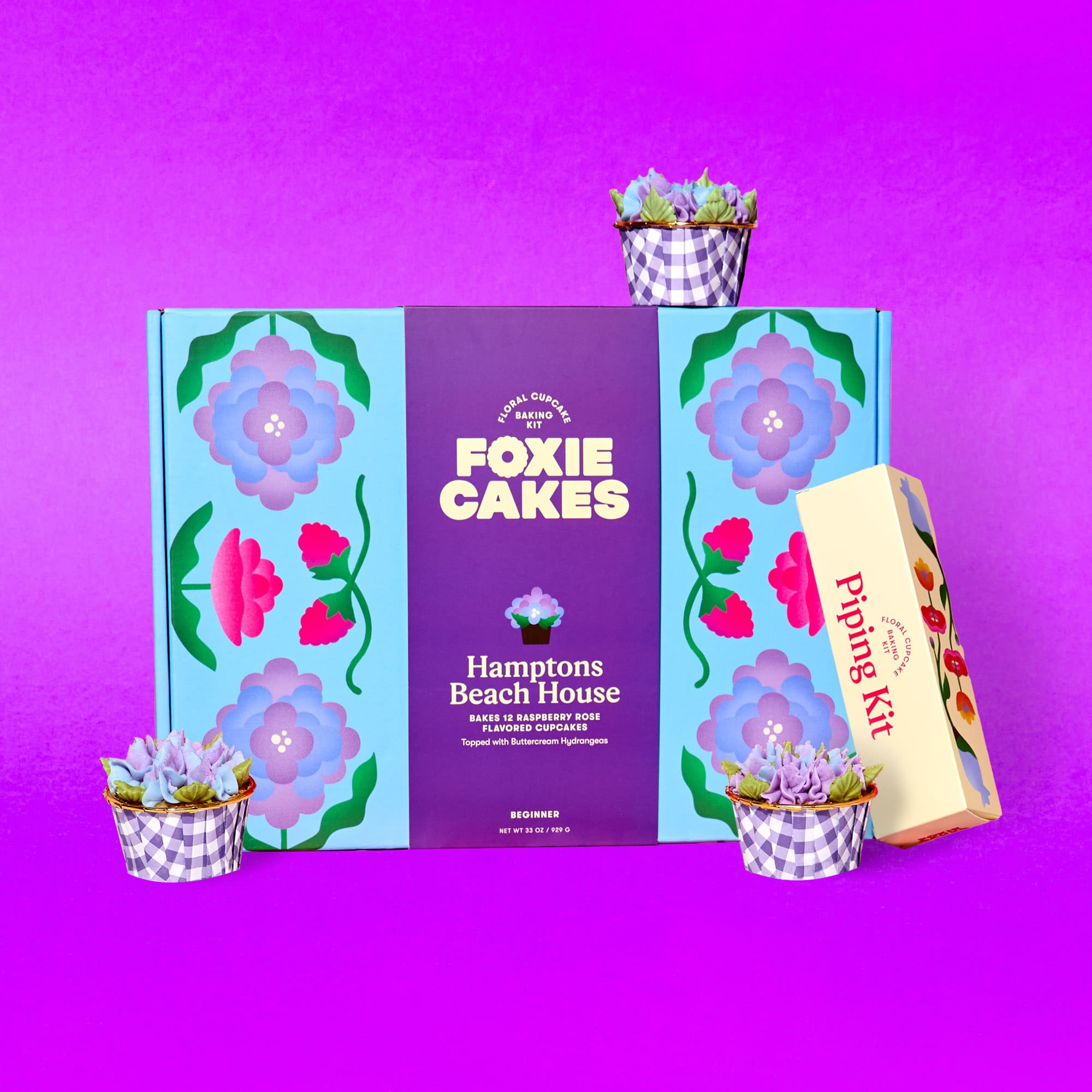 Image of the Better Together Bundle: Foxiecakes Hamptons Beach House floral cupcake baking kit box displayed with expansion piping kit and three decorated raspberry-rose flavor cupcakes featuring hydrangea-style buttercream frosting, on a pink background. Beginner-friendly DIY cupcake decorating kit for a creative at-home baking experience