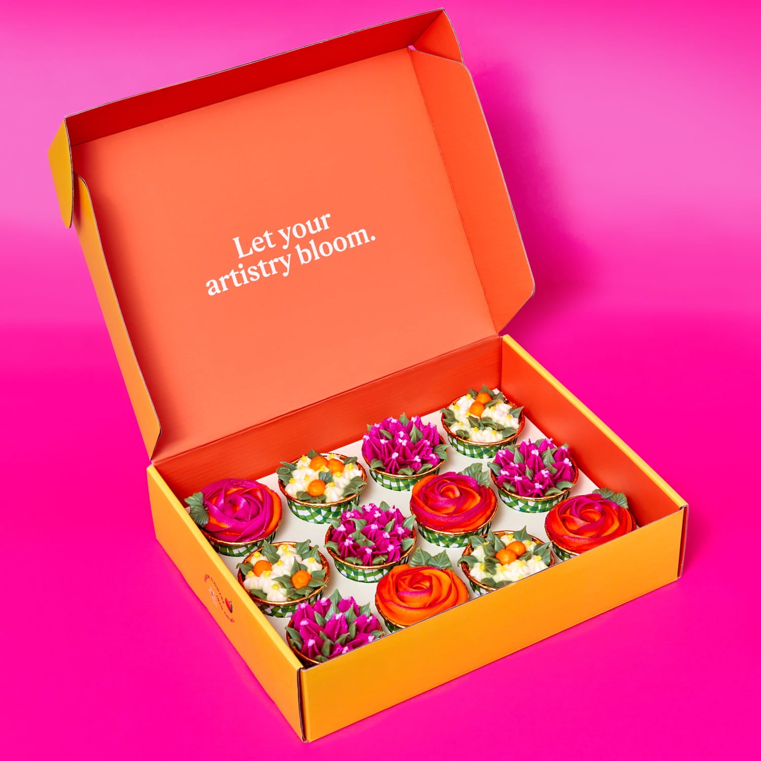 Foxiecakes Arizona Dawn DIY cupcake kit with decorated orange blossom flavor cupcakes topped with rose, bougainvillea and orange blossom-style buttercream in an open box, cupcakes  displayed inside Foxiecakes kit inside carrier. On pink background.