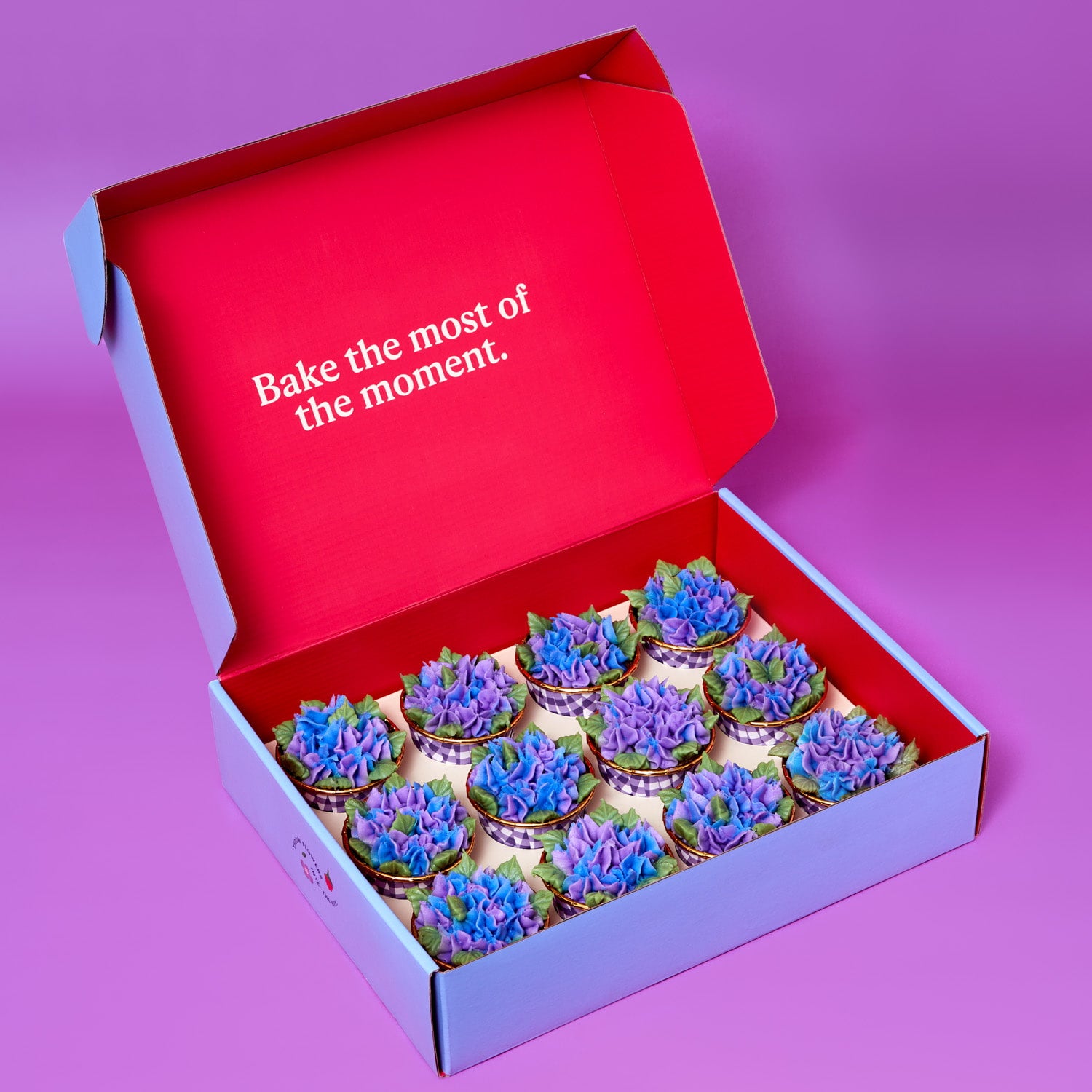 Foxiecakes Hamptons Beach House DIY cupcake kit with decorated raspberry rose cupcakes topped with hydrangea-style buttercream in an open box, cupcakes  displayed inside Foxiecakes kit inside carrier. On purple background.