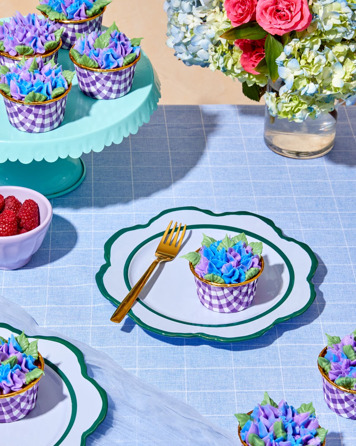 Raspberry rose cupcakes with purple and blue hydrangea buttercream on a styled table setting with pink and blue florals, gold utensils, created using Foxiecakes Hamptons Beach House baking kit
