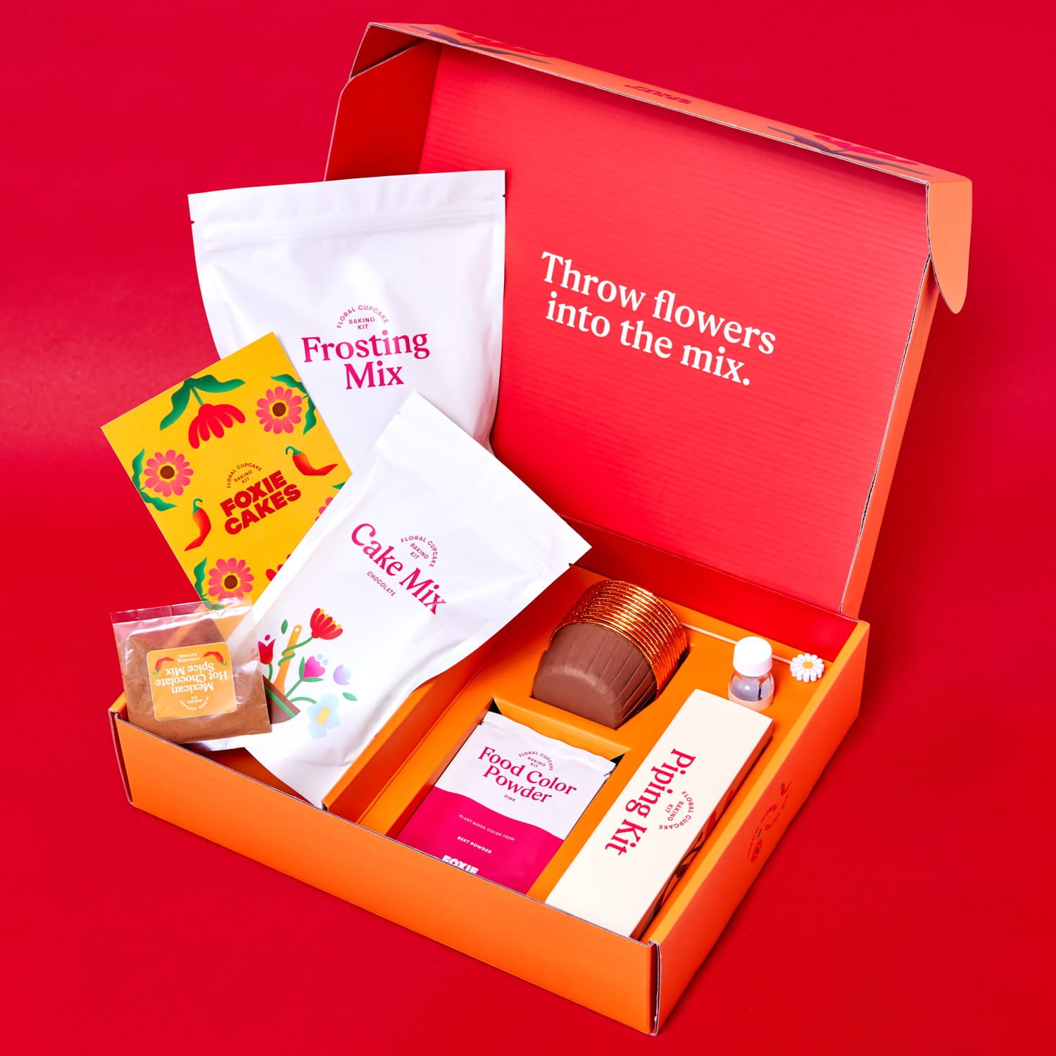 Foxiecakes Oaxaca Campfire floral cupcake kit open box with cake mix, frosting mix, spice mix, food coloring, and piping tools on a red  background