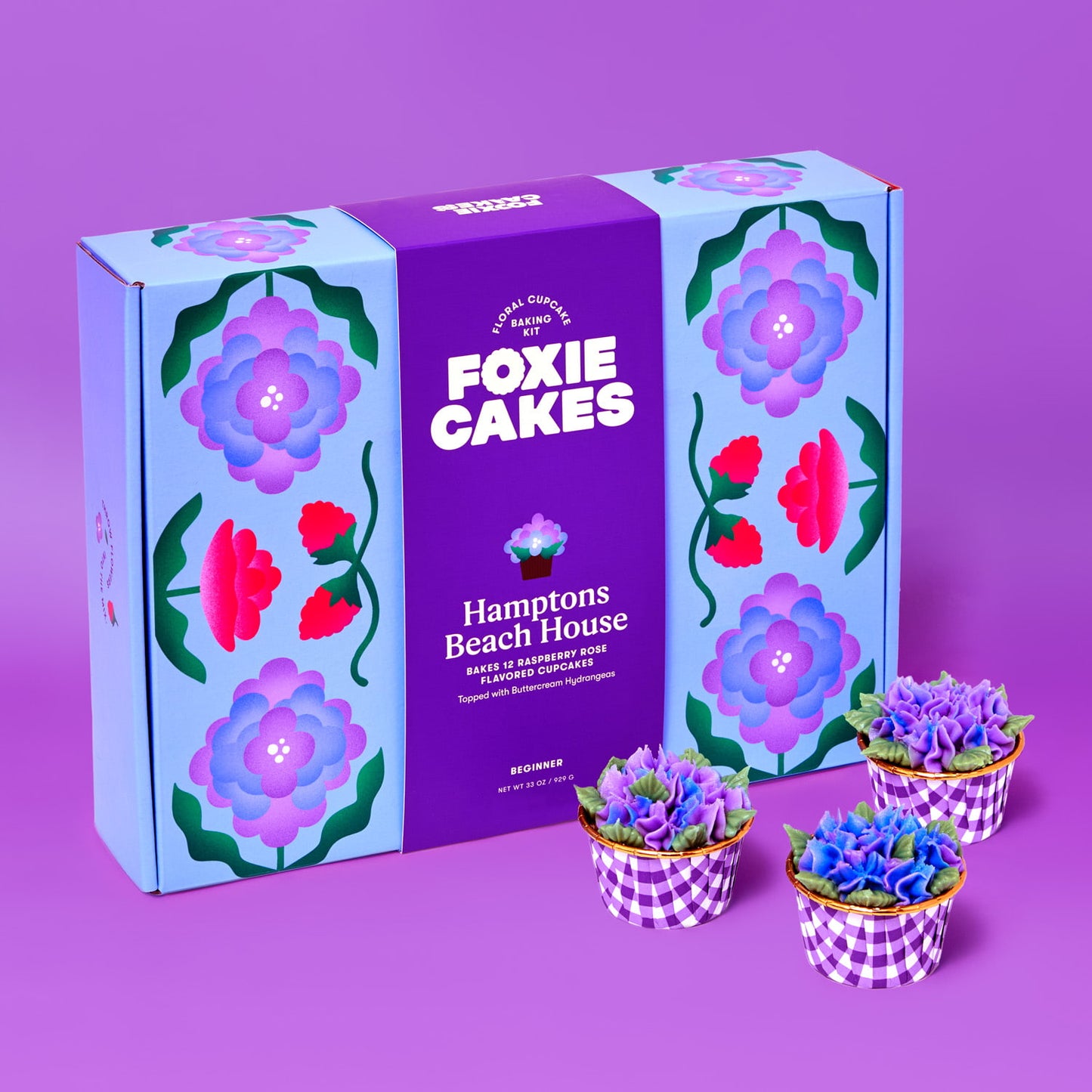 Foxiecakes Hamptons Beach House floral cupcake baking kit box displayed with three decorated raspberry rose cupcakes featuring hydrangea-style buttercream frosting on a purple background, beginner-friendly DIY cupcake decorating kit for a creative at-home baking experience