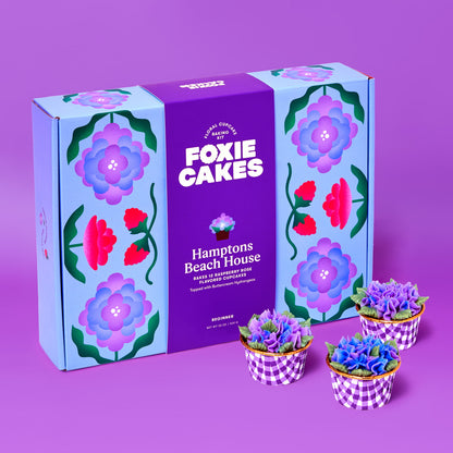 Foxiecakes Hamptons Beach House floral cupcake baking kit box displayed with three decorated raspberry rose cupcakes featuring hydrangea-style buttercream frosting on a purple background, beginner-friendly DIY cupcake decorating kit for a creative at-home baking experience