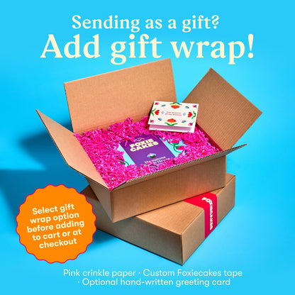 Open cardboard box with pink crinkle paper and a custom Foxiecakes tape and a  floral greeting card on a blue background, with text "Sending as a gift? Add gift wrap! Select gift wrap option before adding to cart or at check out."
