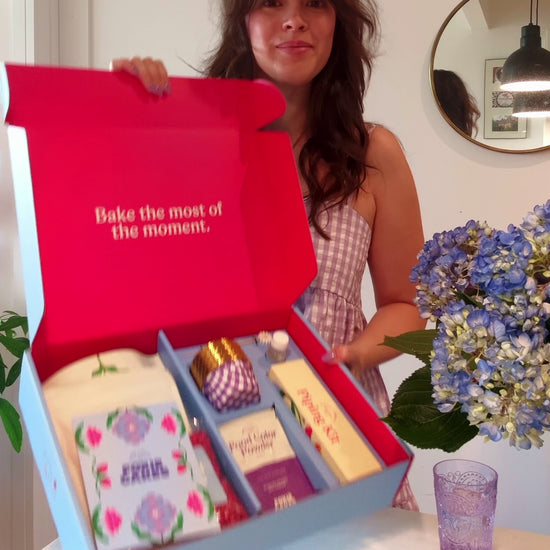 A woman shows the contents of the Foxiecakes Hamptons Beach House Floral Cupcake Baking Kit, including ingredients and tools. She goes through the process of baking and mixing frosting and then pipes hydrangea buttercream flowers onto raspberry-rose cupcakes.