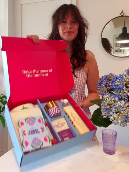 A woman shows the contents of the Foxiecakes Hamptons Beach House Floral Cupcake Baking Kit, including ingredients and tools. She goes through the process of baking and mixing frosting and then pipes hydrangea buttercream flowers onto raspberry-rose cupcakes.